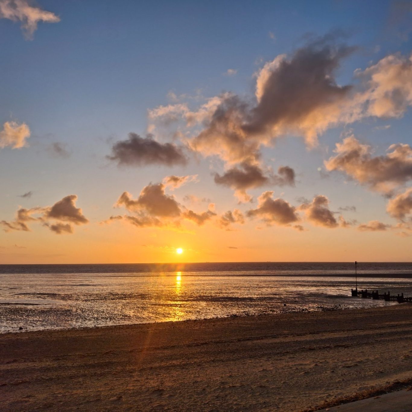 A beach sunset A serene beach at sunset with golden light reflecting on wet sand and water, scattered clouds, and an open horizon under a glowing sky.