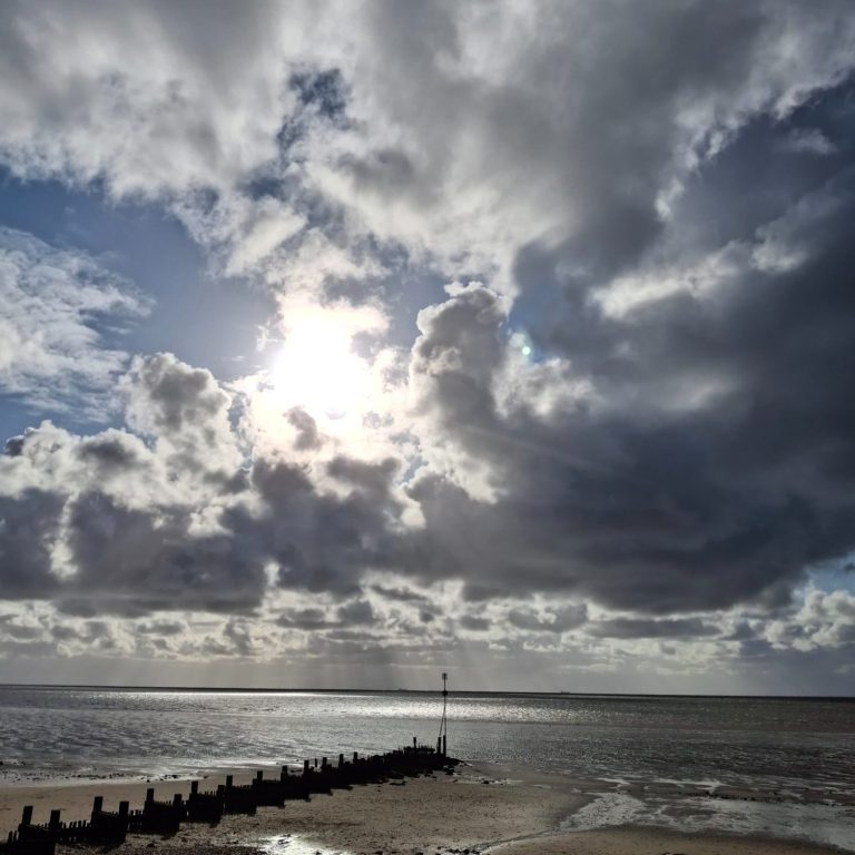 Beach with dramatic sky A dramatic beach scene with dark clouds, sunlight breaking through, wet sand, scattered rocks, and a wooden groyne stretching into the water